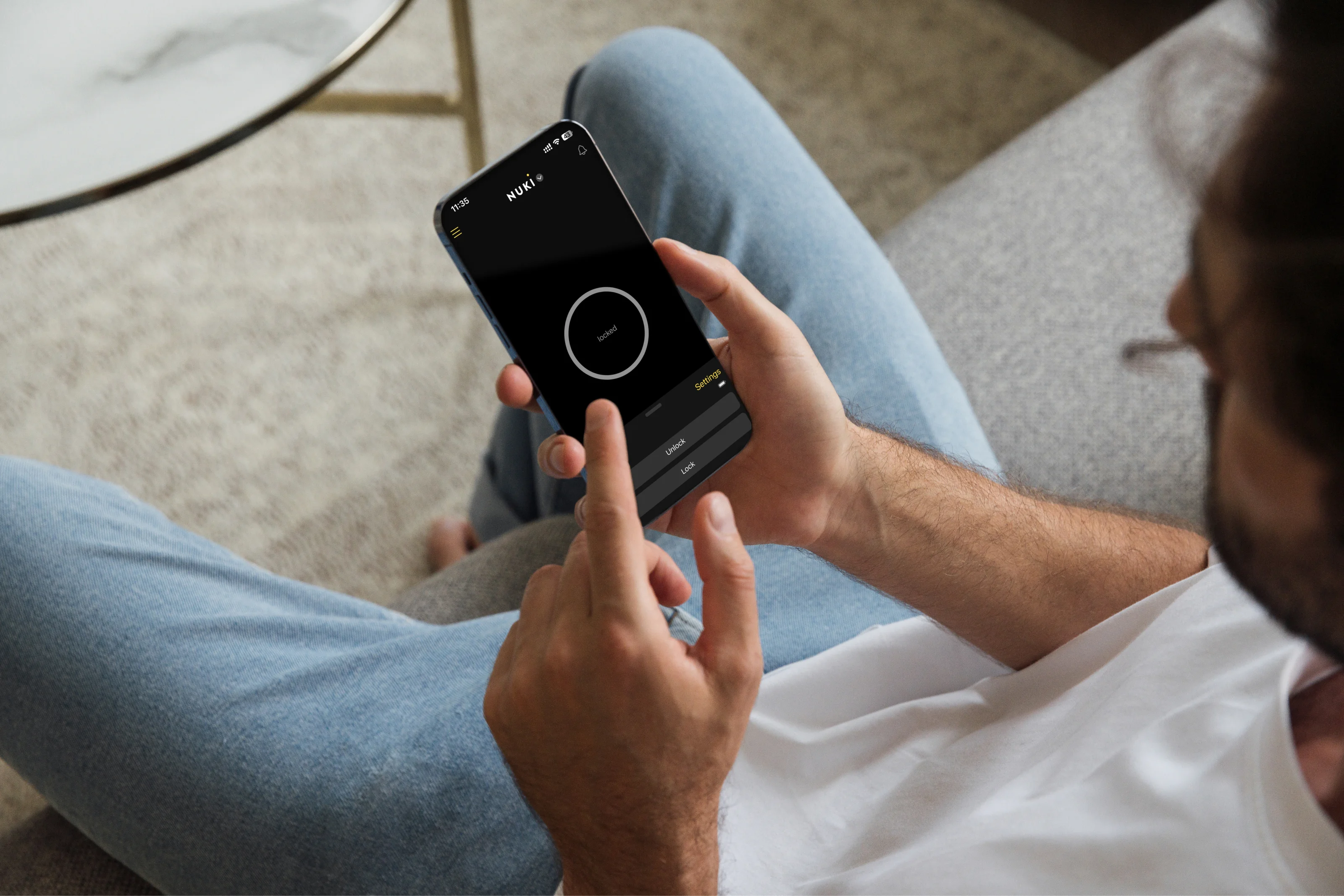 Person sitting on a couch using the Nuki app to unlock the door with a smartphone.