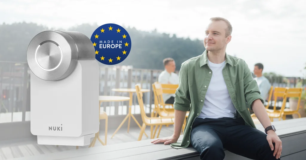 Il Nuki Smart Lock Go con un badge “Made in Europe”. Sullo sfondo, un uomo in un bar.