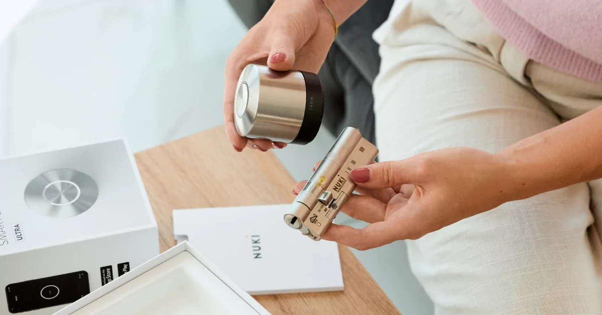 A woman sits at a table and holds a freshly unpacked Smart Lock Ultra and the included universal cylinder.
