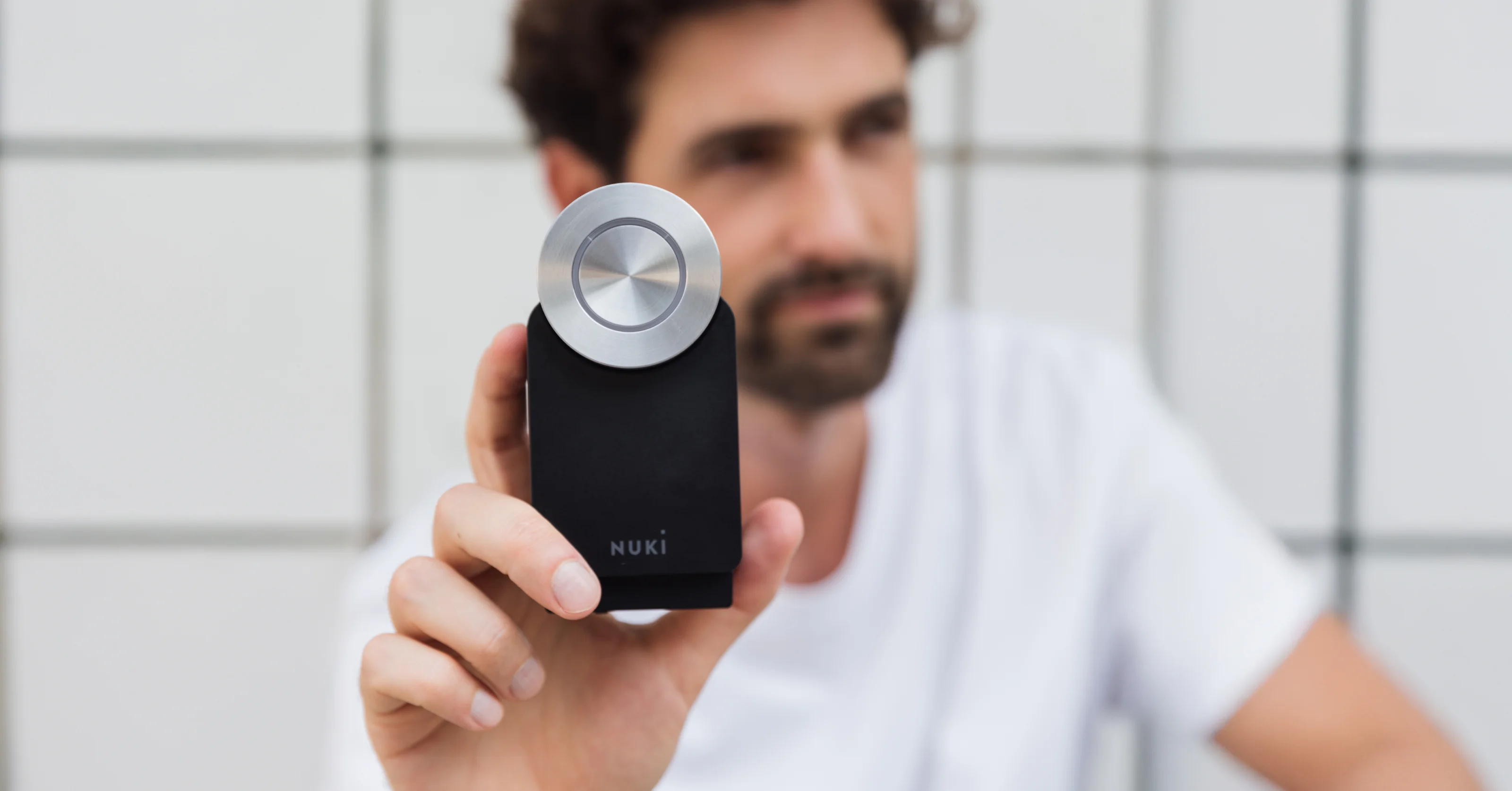 Un uomo sullo sfondo tiene in mano la Nuki Smart Lock di 4ª generazione.
