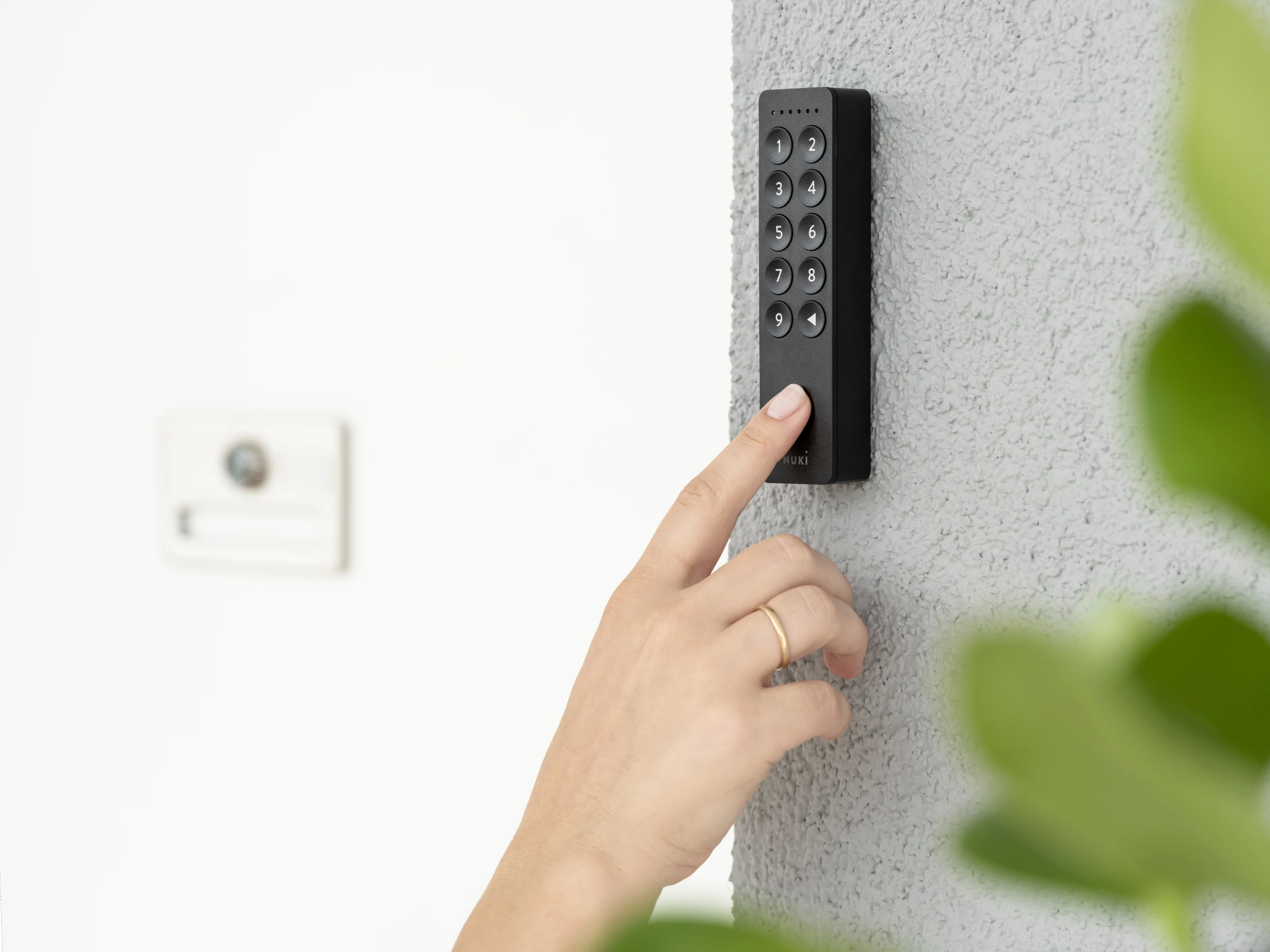 Mano con anello che usa un keypad su un muro esterno grigio.