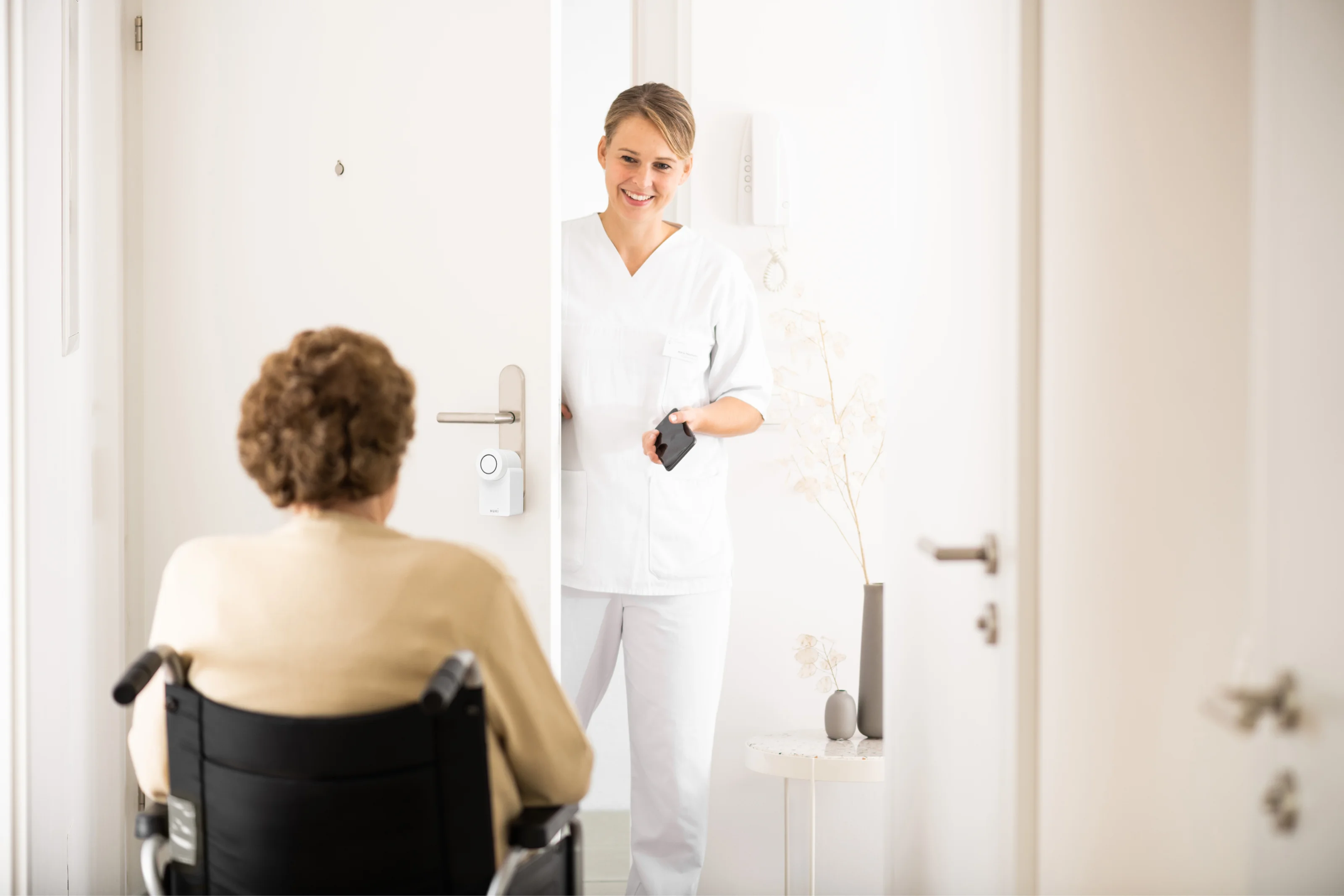 Assistente apre la porta con lo smartphone tramite uno smart lock; all’interno, persona in sedia a rotelle.