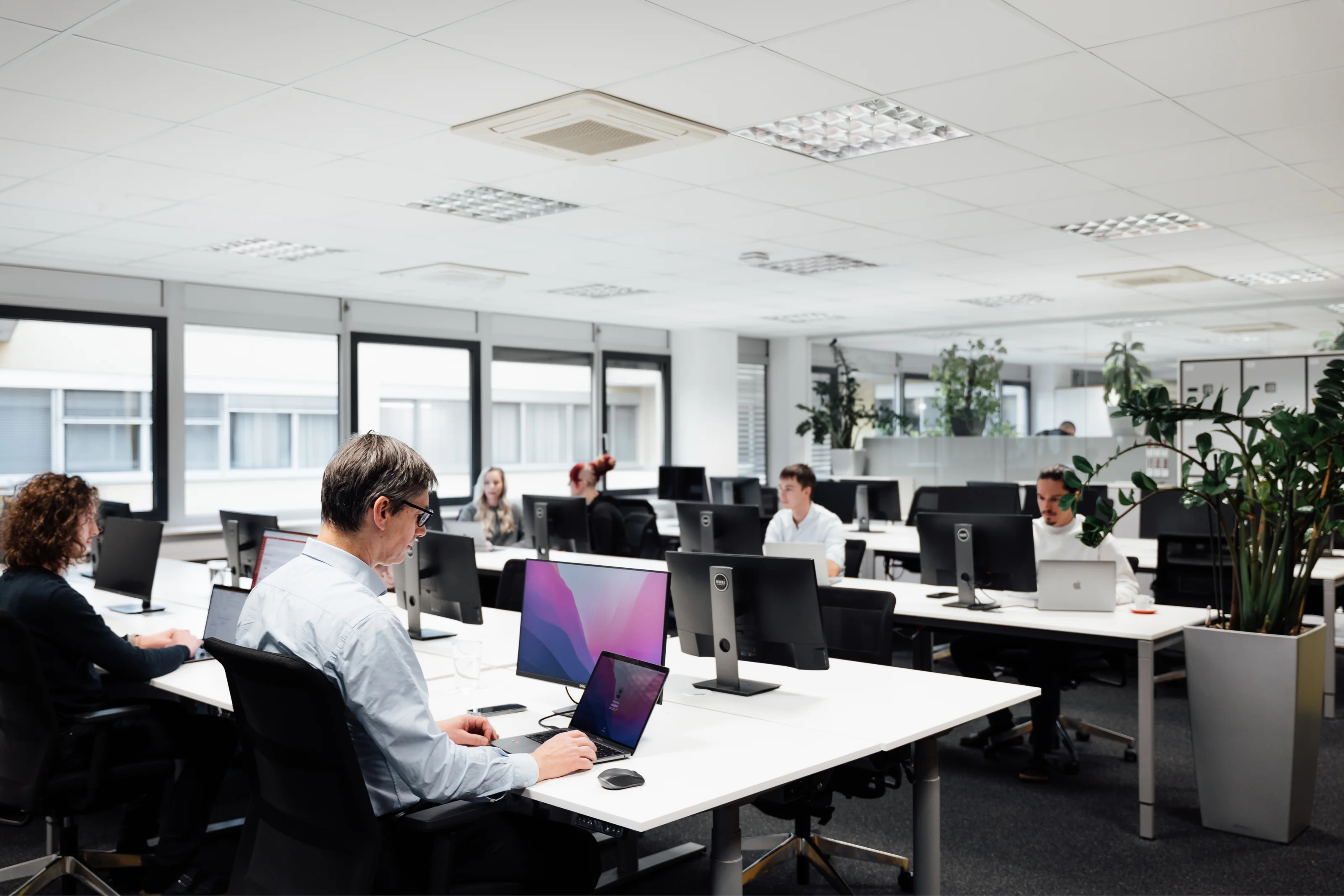Ufficio open space con persone che lavorano al computer in un ambiente moderno e luminoso.