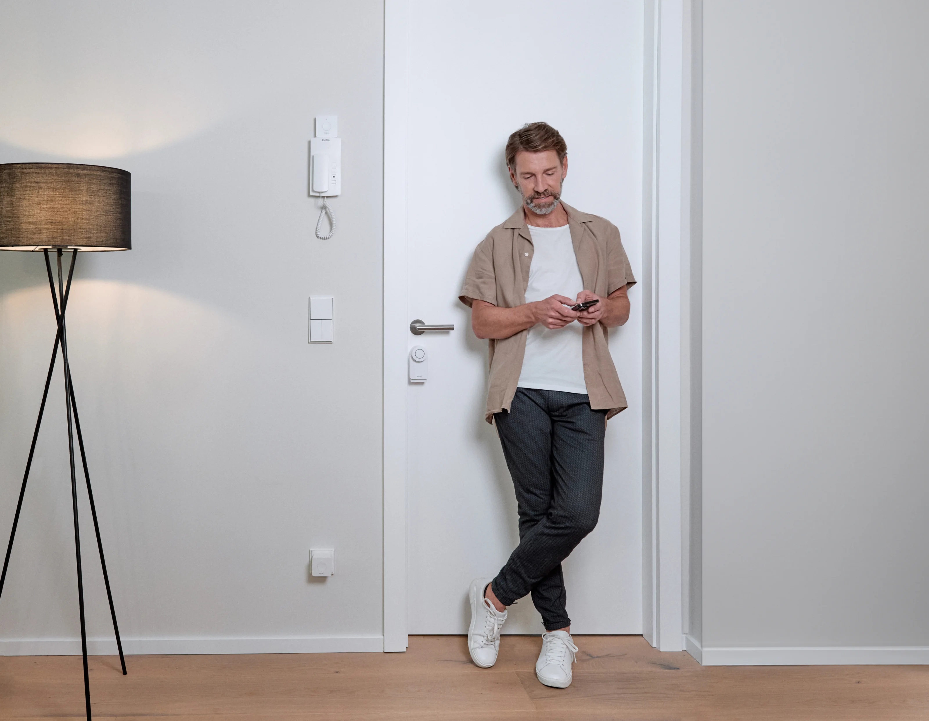 Un homme devant la porte d'entrée avec la Smart Lock dessus installe l'application Nuki sur son smartphone.