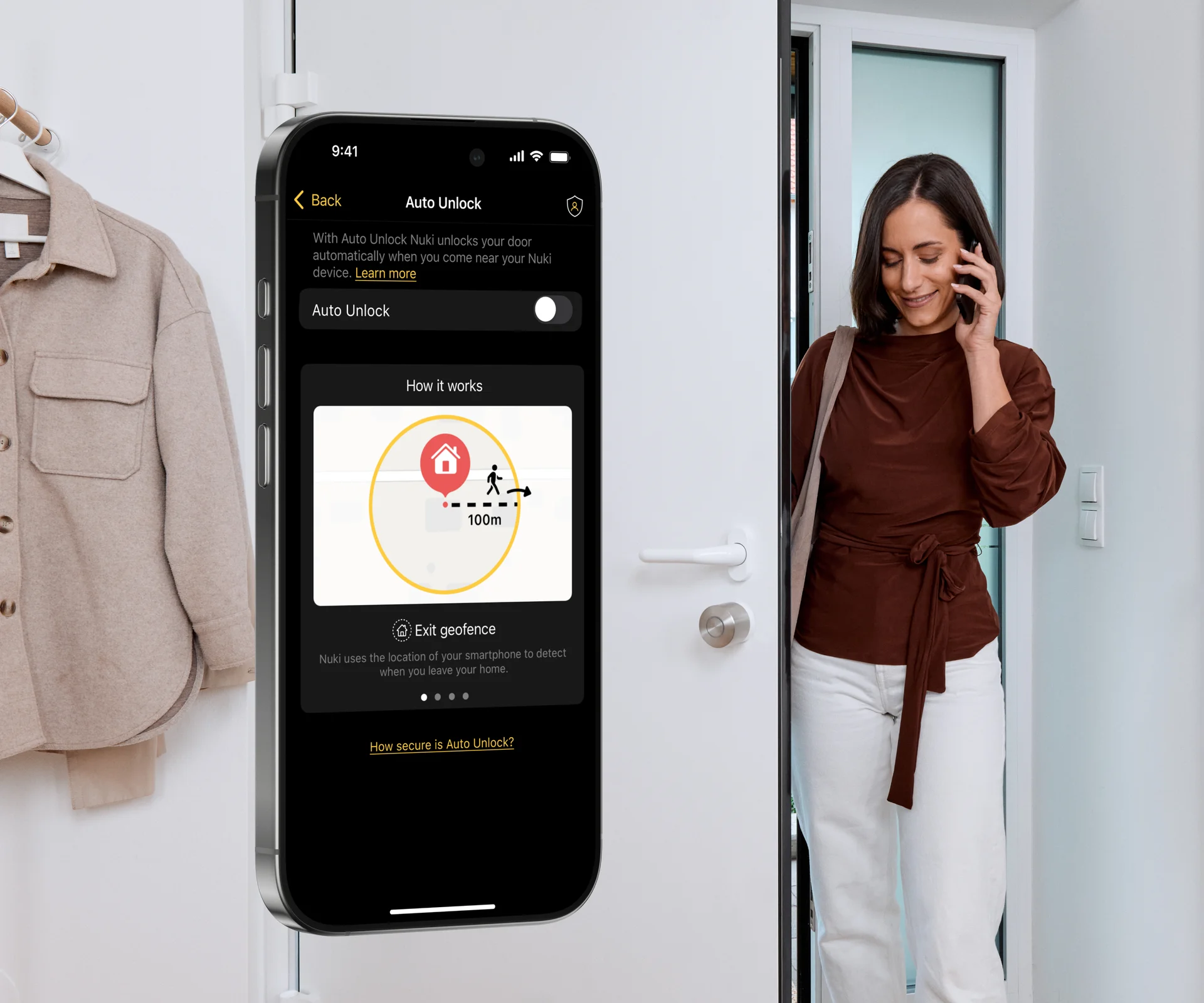 Una donna entra dalla porta d’ingresso. La Smart Lock è montata all’interno della porta. L’app Nuki con le impostazioni di Auto Unlock è visibile su uno smartphone.