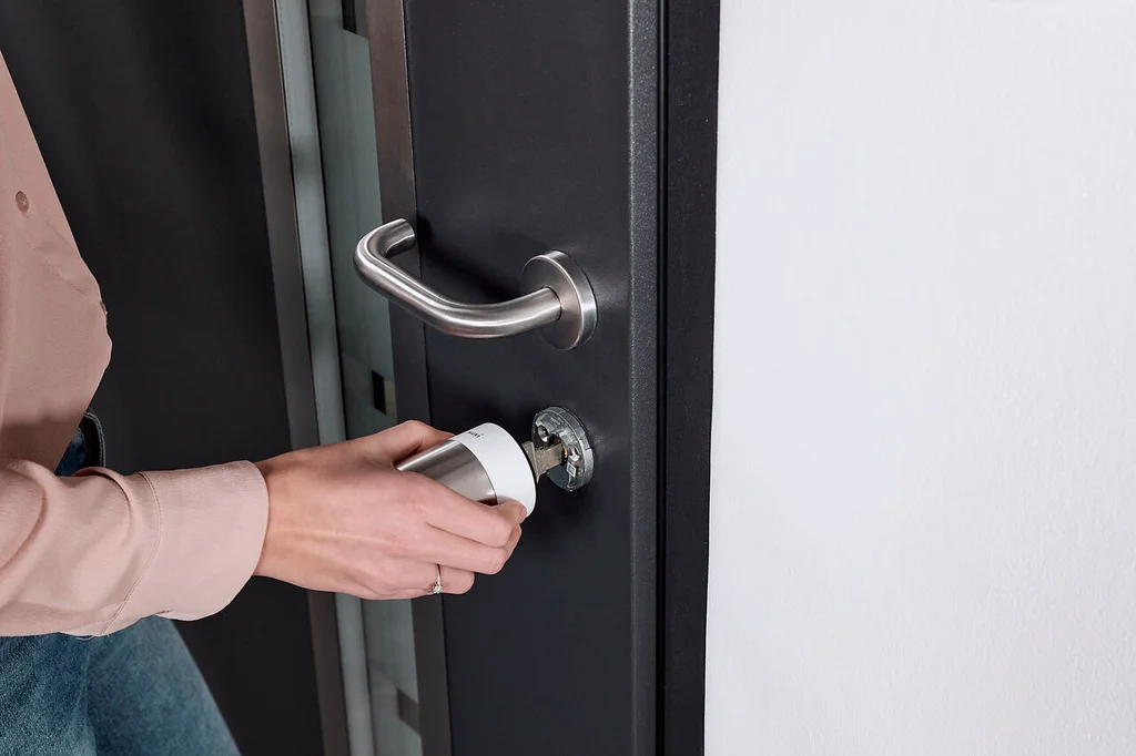 Donna installa la Nuki Smart Lock Pro bianca su una porta scura con ferramenta argento.