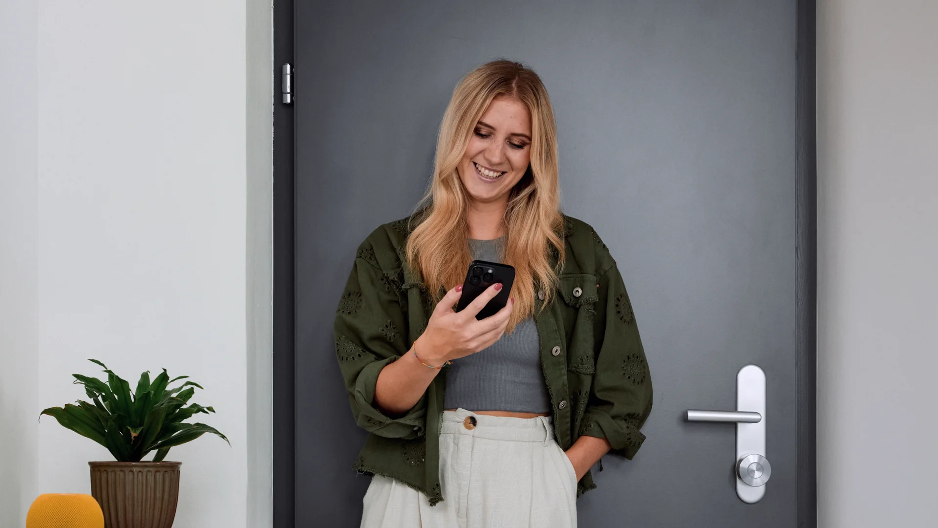 Donna davanti alla porta, sorride mentre usa l’app Nuki – accesso smart con un tocco.