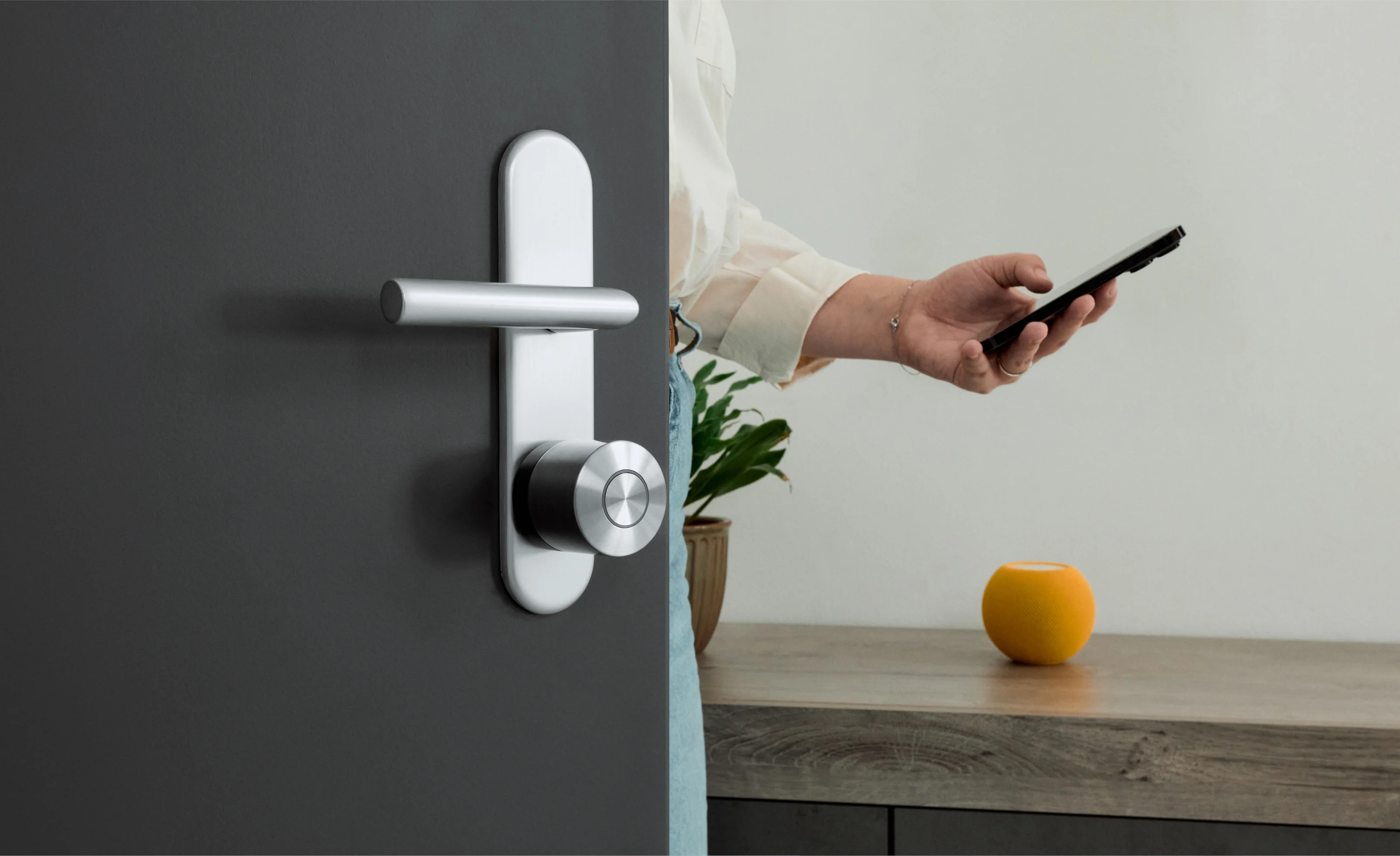 Femme entrant dans une pièce par une porte noire avec la Nuki Smart Lock Ultra. Un HomePod mini est sur le meuble.