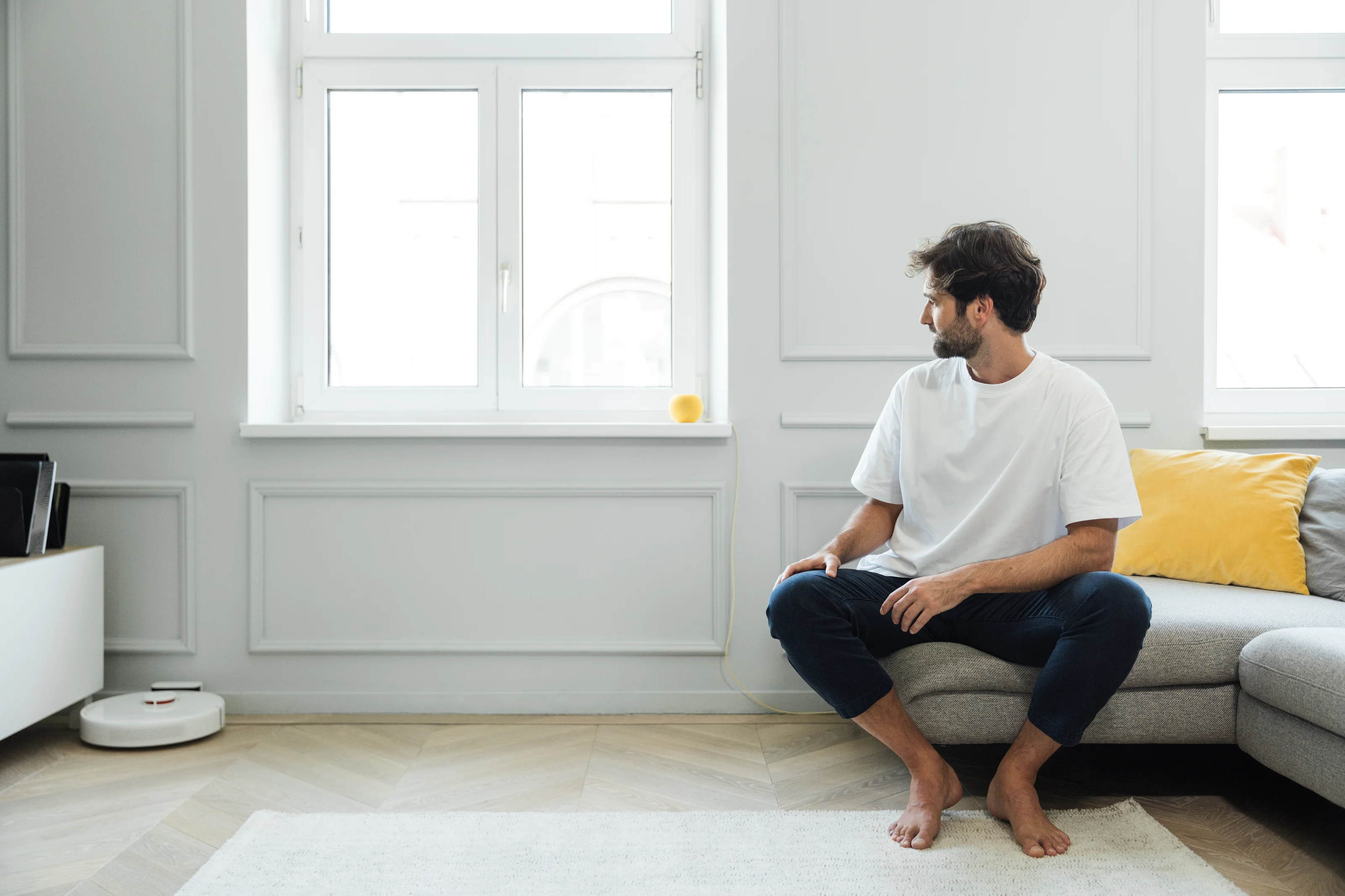 Uomo seduto sul divano nella sua smart home mentre guarda uno smart speaker.
